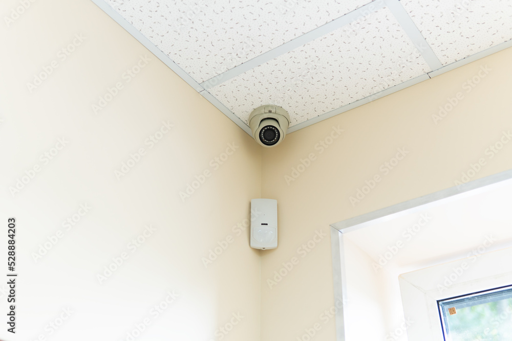 Aufkleber security camera and motion detector installed on ceiling in room.