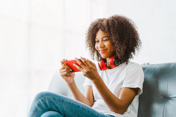 Fototapeta Excited cheerful gen Z female using mobile phone getting surprising good news while playing mobile game on sofa. obraz