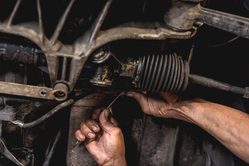 A mechanic inspecting or fixing the steering rack underneath the car at an auto repair shop.