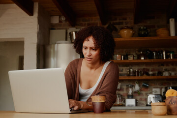 Young biracial woman concentrating while working on laptop in kitchen at home