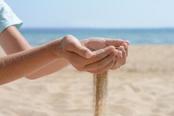Child pouring sand from hands on beach near sea, closeup. Fleeting time concept