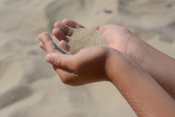 Child pouring sand from hands outdoors, closeup. Fleeting time concept