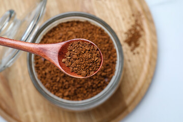 Spoon of instant coffee over jar on wooden tray, top view