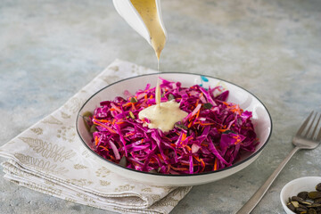 Coleslaw salad of red cabbage and carrots with mayonnaise dressing in a white bowl on a gray concrete background. Vegan Recipes.