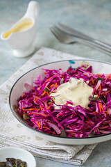Coleslaw salad of red cabbage and carrots with mayonnaise dressing in a white bowl on a gray concrete background. Vegan Recipes.
