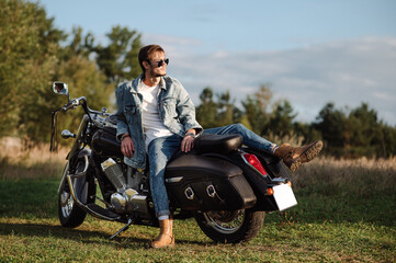 Handsome male biker wearing a jeans clothes is sitting on the motor bike