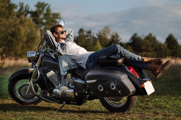 Fototapeta na wymiar Handsome male biker wearing a jeans clothes is sitting on the motor bike