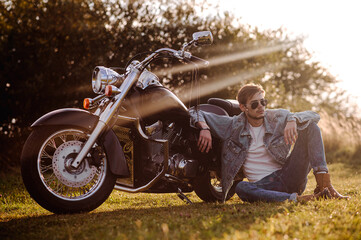 Young male biker in sunglasses is sitting on the groung with a motor bike