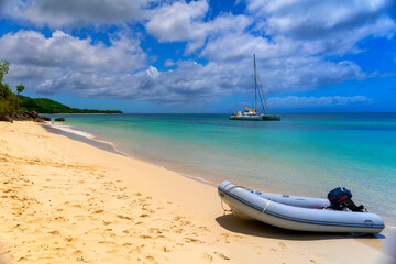 Paradise caribbean beach with golden sand and turquoise water. A small inflatable boat in the foreground and a catamaran in the sea.