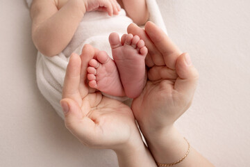 The palms of the parents. A father and mother hold the feet of a newborn child in a white blanket...