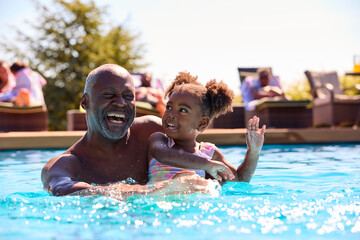 Grandfather Teaching Granddaughter To Swim In Outdoor Pool On Holiday