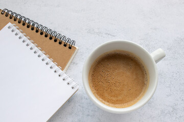 Cup of cappuccino coffee, spiral notebook and kraft paper sketchbook on office table background. Top view, flat lay, copy space. Stationery supply for art, education and work. Blank page, mock up. 