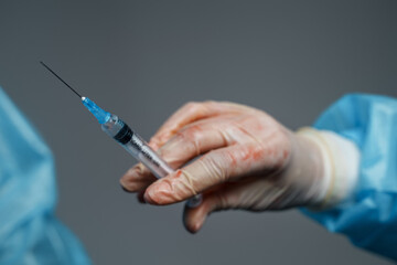 Closeup shot of surgeon specialist with injector and white rubber gloves against gray background.