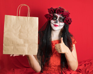 Portrait of a young woman in a red dress and traditional sugar skull makeup for the celebration of Dia de los Muertos, the Day of the Dead