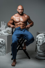 Fototapeta na wymiar Studio shot of handsome guy with naked torso and muscular build around greek busts.