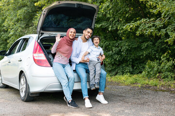 Family journey at weekend at own auto. Glad millennial arab man and woman in hijab holding baby