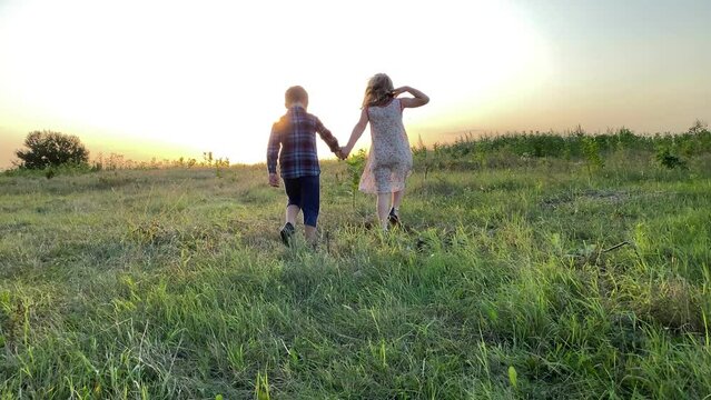 Silhouette little kids walking skipping on meadow forward golden lights of summer sunset. Cheerful girl, cute boy having fun at countryside. Lovely children enjoying pastime at nature. Simple living