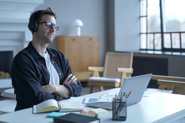 Positive German man bank employee sitting at workplace at modern home office in wireless headphones