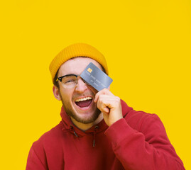 Young guy with credit or debit card in hand happy smiling cover his eye ready to spend money. Young...