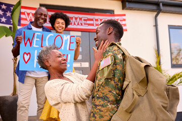 Multi-Generation Family With Parents And Wife Welcoming Army Soldier Home On Leave With Banner