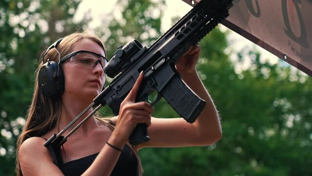 White brunette woman in protective gear firing submachine gun on training ground. Aim practise. Horizontal outdoor shot. High quality 4k footage