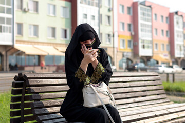 Fototapeta premium A Muslim woman is resting on a bench in the park, tidying herself up looking in a mirror.