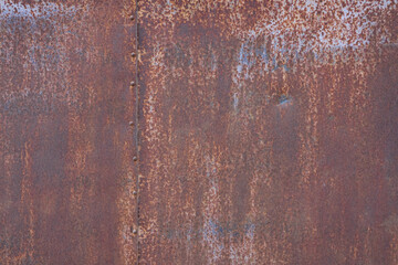 Fragment of a metal wall with a rusty surface. There is a connection of two sheets with rivet heads. Background. Grunge. Texture.