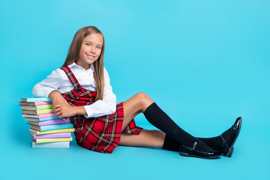 Full length photo of young little cute schoolgirl sitting hold books library reader isolated on blue color background