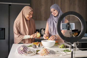 Two muslim content creators slicing, chopping and peeling vegetables at kitchen to prepare a salad.