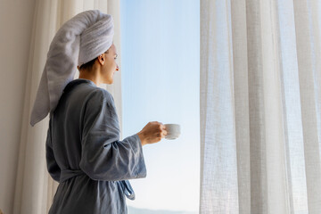 Relaxed woman wearing bath robe drinking coffee in hotel room in morning
