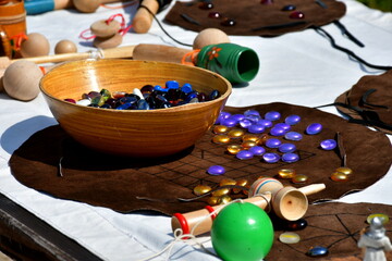 A close up on a table full of medieval games and accesories, such as a bowl with a lot of colorful, vivid marbles, wooden toys, some chess set and other items seen on a sunny summer day in Poland