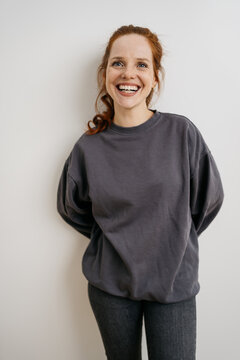 happy young redhead woman in front of a white wall and looks into the camera