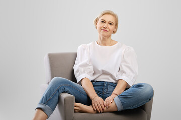 Positive mature woman sitting in an armchair in studio