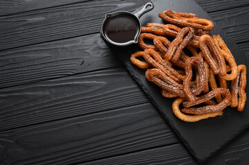 Homemade churros with chocolate on a dark wooden rustic background.