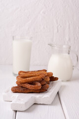 Homemade churros with milk and cream on a white wooden background.
