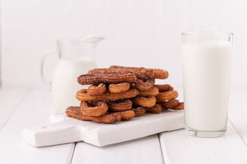 Homemade churros with milk and cream on a white wooden background.