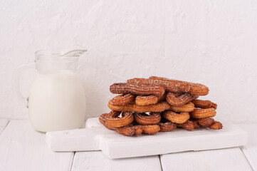 Homemade churros with milk and cream on a white wooden background.