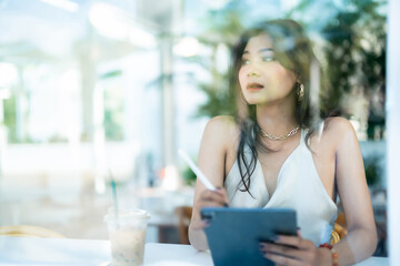 beautiful asian freelance Success people business woman fashion model in summer white sleeveless dress using casual working with tablet for browsing internet, chatting and blogging in coffee shop.