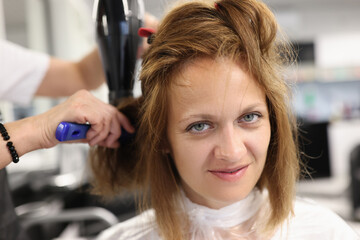 Fototapeta premium Woman hairdresser dries and straightens client hair with comb and hair dryer in beauty salon