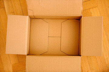 Open empty cardboard parcel on the wooden parquet floor - delivery concept unboxing unpacking