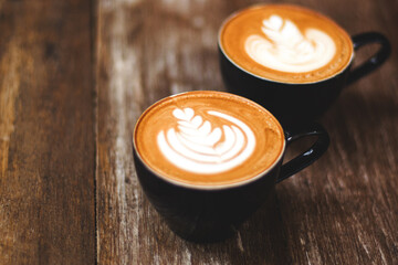 Two cups of cappuccino with beautiful latte art on wooden table background.