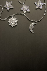 Silver garland with decorations in the shape of the moon, stars and sun on a dark background with copy space