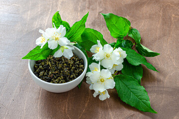 jasmine tea dry for brewing in a cup and sprigs of flowering jasmine on a wooden table, herbal healthy tea