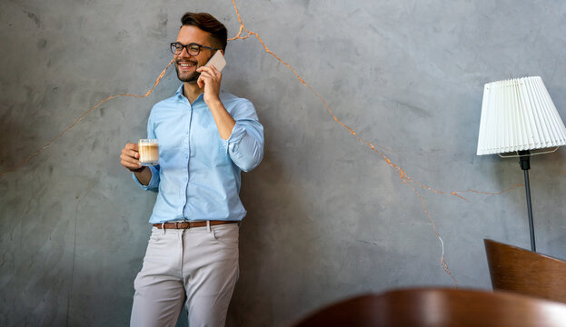 Portrait of a smiling young business man using smartphone and holding cup of coffee