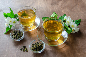 two cups of jasmine tea and brewing on a wooden table next to sprigs of jasmine with leaves and flowers, herbal tea medicinal dietary