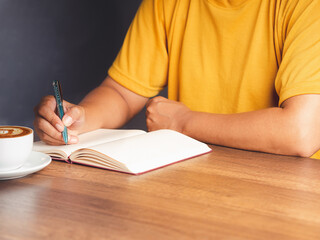 Close-up of hand holding a pen writing on a notebook on the desk