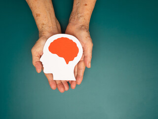 Top view of head with a brain made from paper on the palm senior woman over a green background