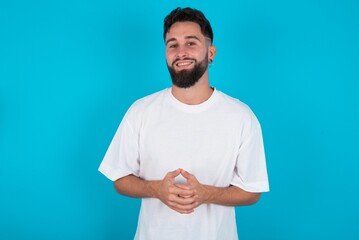 Business Concept - Portrait of bearded caucasian man wearing white T-shirt over blue background holding hands with confident face.