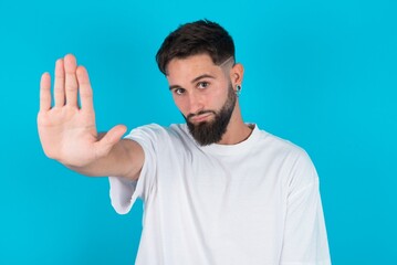 Fototapeta premium bearded caucasian man wearing white T-shirt over blue background doing stop gesture with palm of the hand. Warning expression with negative and serious gesture on the face.