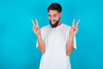 bearded caucasian man wearing white T-shirt over blue background with optimistic smile, showing...